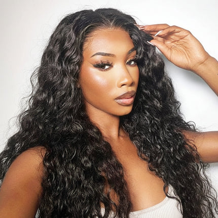 Woman with long, wavy black hair styled in a wig, wearing a white top against a light gray background.